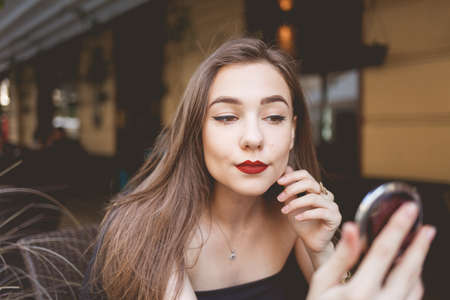 Portrait of a beautiful girl with a mirror in her hands sitting at a cafe tableの写真素材