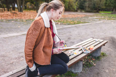Portrait of a young artist girl who sits on a bench and draws a pictureの写真素材