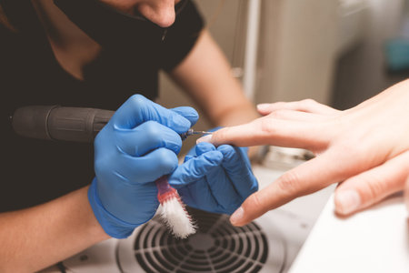 Manicurist cleans nails with a nail file drill before applying varnish