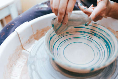Professional potter works on painting plates in the workshop. Woman paints a ceramic plate with a brush and blue paintの写真素材