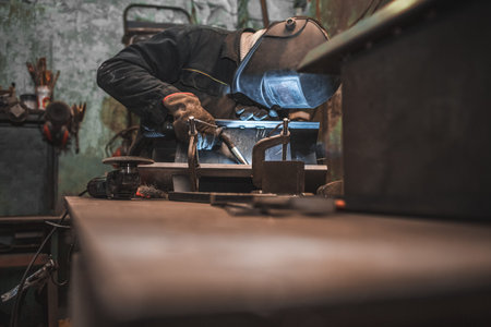Worker in a welder mask works in a workshop for welding iron. Man makes iron products. Guy works...