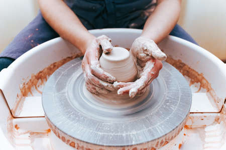Process of creating and formation a white clay ceramic plate. Professional potter is engaged in modeling clay plates. Potter works in a workshopの写真素材
