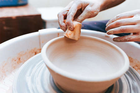 Process of creating and formation a white clay ceramic plate. Professional potter is engaged in modeling clay plates. Potter works in a workshopの写真素材