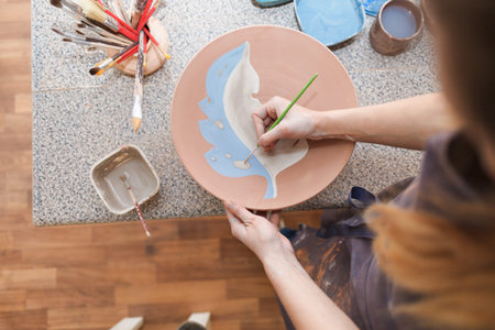 Potter woman paints a ceramic plate. Girl draws with a brush on earthenware. Process of creating...