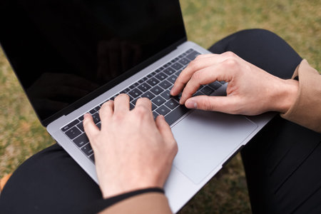 Man works at a laptop while sitting on the grass