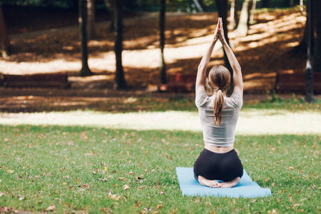 Girl doing yoga in the park on the mat. Yoga exercise outdoor.