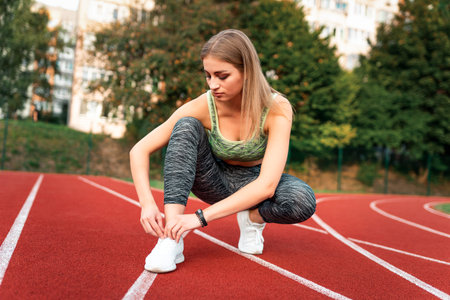 Beautiful female runner tying shoelaces in the running track