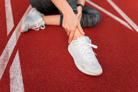 Sports girl injured her ankle and holding her leg while sitting on the stadium trackの写真素材
