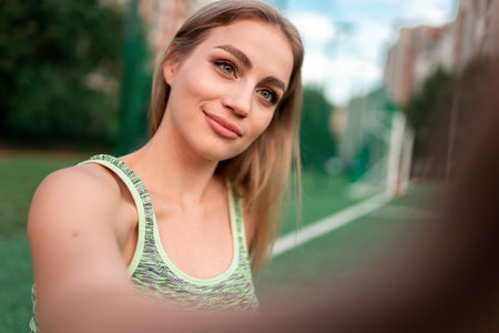 Athletic girl makes a selfie while sitting on the lawn of a football field