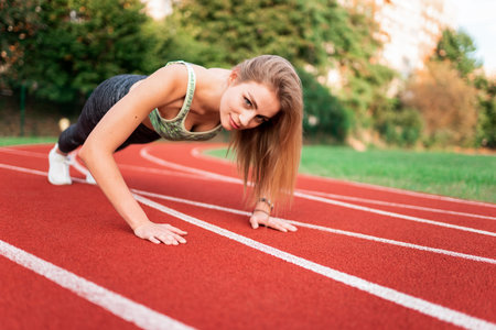 Athletic girl stands in the plank at the stadium runway
