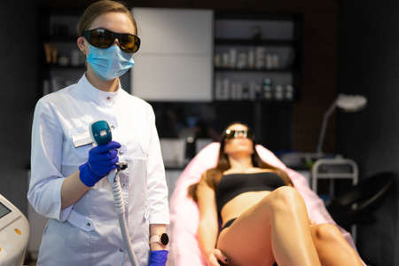 Cosmetologist with laser in hands is ready to do hair removal for a clientの写真素材