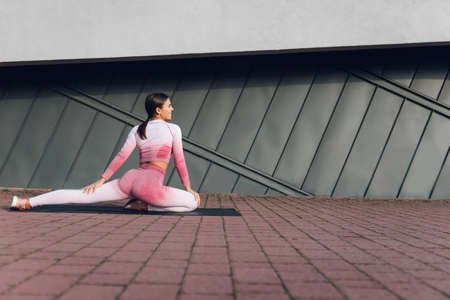 Female with a beautiful figure is stretched while sitting on mat near the wallの写真素材