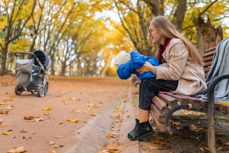 Joyful mother playing with little baby while sitting on bench in the park