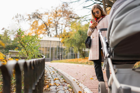 Mom with stroller walks in the park and texting on the phone. Smartphone addiction concept