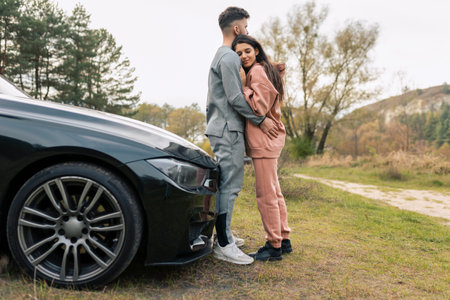 Romantic Ñouple dressed in tracksuits hugs while standing near car in natureの写真素材