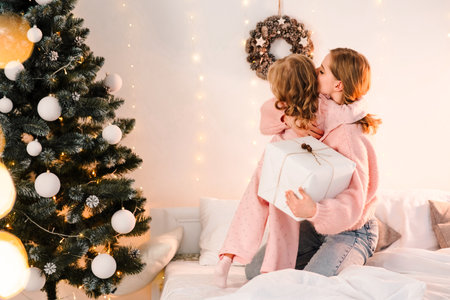 Little daughter hugs mom on bed and thanks for christmas giftsの写真素材