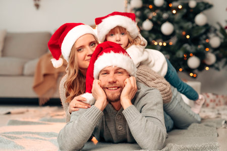 Happiness family lies on the floor in Christmas hats against the background of decorated Christmas treeの写真素材