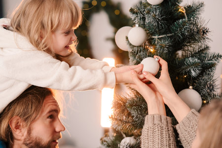 Happy family with child decorate christmas tree. Little girl sitting on daddy's shoulders hangs ball on the Christmas treeの写真素材