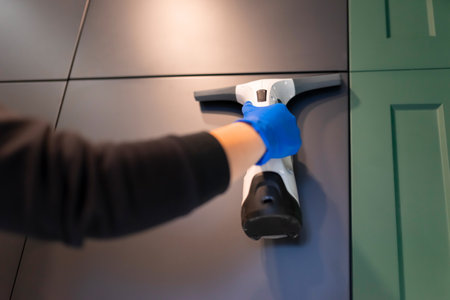 Ceaning company employee cleans kitchen cabinets with window vacuum cleanerの写真素材