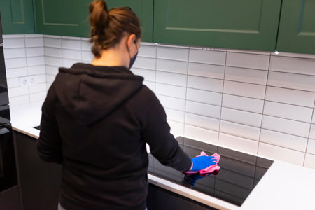 Woman cleans the kitchen and wipes the induction hob with microfiber. House cleaning processの写真素材