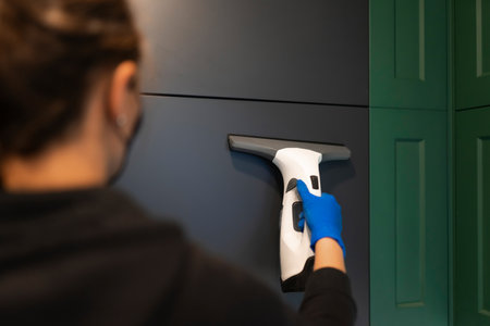 Cleaning company employee cleans kitchen cabinets with window vacuum cleanerの写真素材