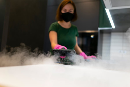 Woman employee cleaning company blows vapor out of steam generator. Steam cleaning process for kitchen furnitureの写真素材