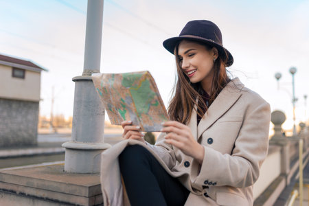 Tourist woman sits and looks at map of the city. Girl prefers to use paper map for orientation in the cityの写真素材