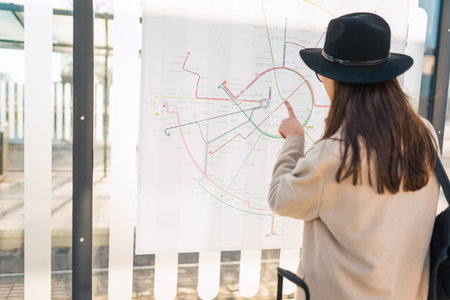 Female tourist looking the routes map at the bus stop. Stylishly dressed woman traveler looks at the...