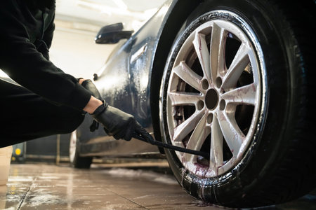 Detailing center worker cleans car wheels with brush. Vehicle wheel rim cleaning processの写真素材