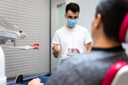 Dental surgeon with dental crown in hands model talks to patient about prosthetics. Man at the dentist's appointmentの写真素材
