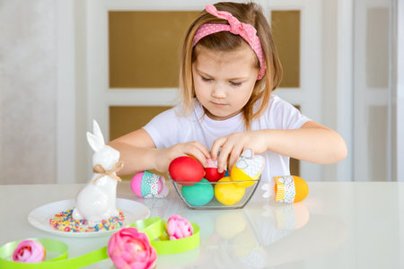 Little girl sitting at the table and decorating Easter eggs