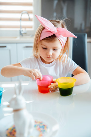 Little girl paints eggs for easter holidays. Child creates festive decorationsの写真素材