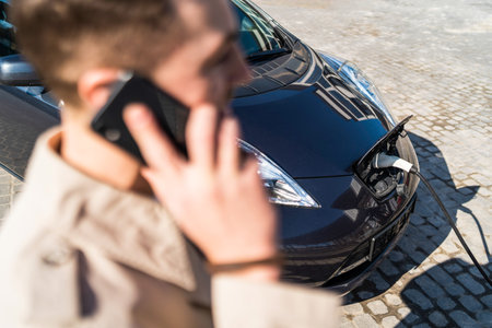 Man talks on the phone while his car is charging at the station