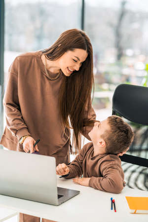 Mother smiles to her son who is sitting at laptopの写真素材