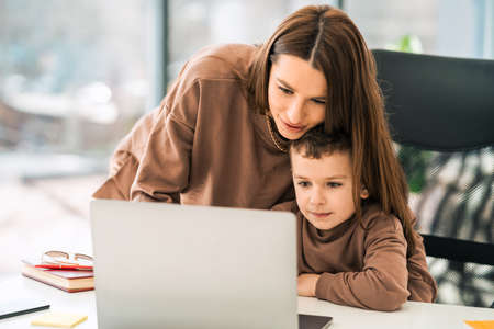 Loving mom helps son with homework while sitting at laptop. Woman with a little boy at computerの写真素材