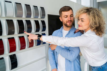 Family couple in car dealership choosing the color of their new car. Man and woman looking color samples of car bodyの写真素材