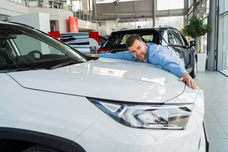 Handsome man hugging new car in dealershipの写真素材