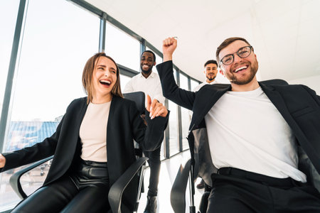 Joyful employees ride on chairs around the office celebrating the end of the working weekの写真素材