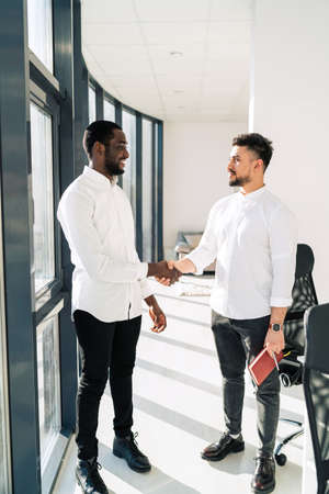 Two multiracial businessmen shake hands in officeの写真素材
