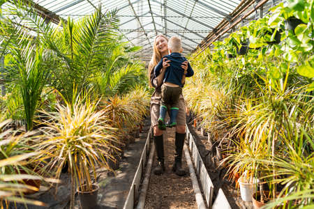 Joyful mother picks up her son while walking in the greenhouseの写真素材