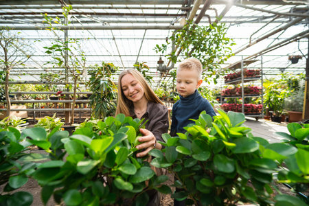 Woman greenhouse worker with her little son caring for plants in the greenhouse
