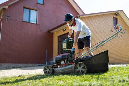 Gardener with a can of gasoline in his hands unscrews the fuel cap of a lawn mowerの写真素材