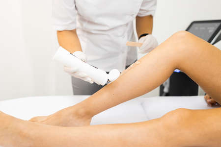 Beautician applies a special gel for laser hair removal to a woman's legの写真素材