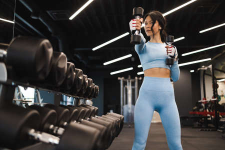 Beautiful fitness woman in blue sportswear exercising with dumbbellsの写真素材