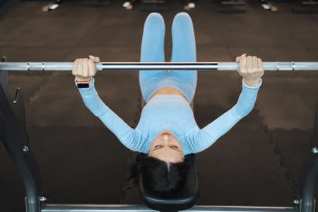 Woman lifts a barbell while lying on a benchの写真素材