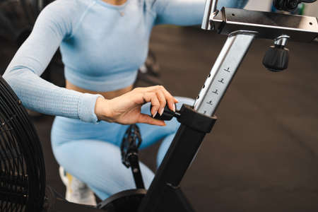 Sportswoman adjusts the height of the exercise bike seat before starting a workoutの写真素材