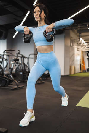 Attractive woman in blue sportswear working out with kettlebell at the gymの写真素材