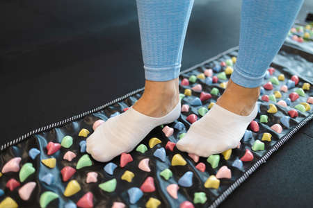 Acupuncture points of the foot stimulation. Woman stand on orthopedic foot massage mat. Massage rug with colorful stonesの写真素材