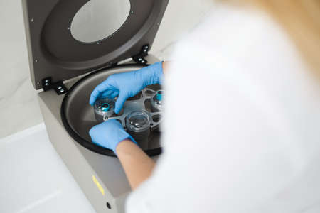 Cosmetologist puts metal container with test tubes in a centrifugeの写真素材