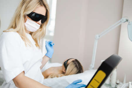 Female laser hair removal specialist in protective glasses prepares epilator for procedureの写真素材